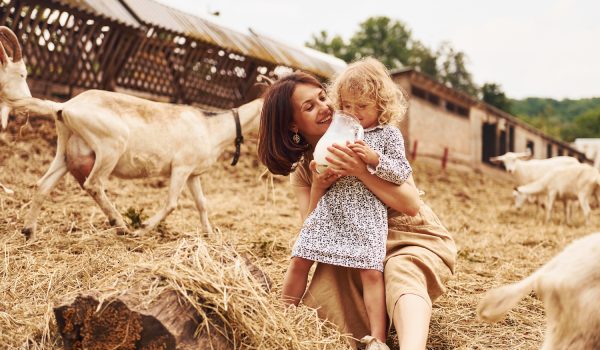 Young mother with her daughter is on the farm at summertime with goats.